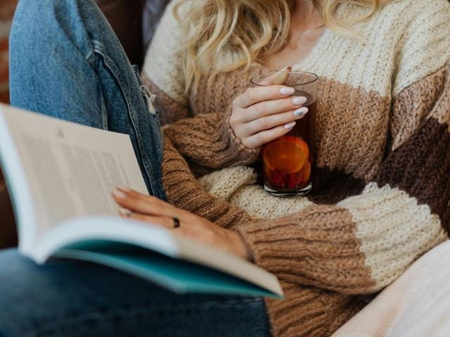 kvinde læser en bog og drikker te